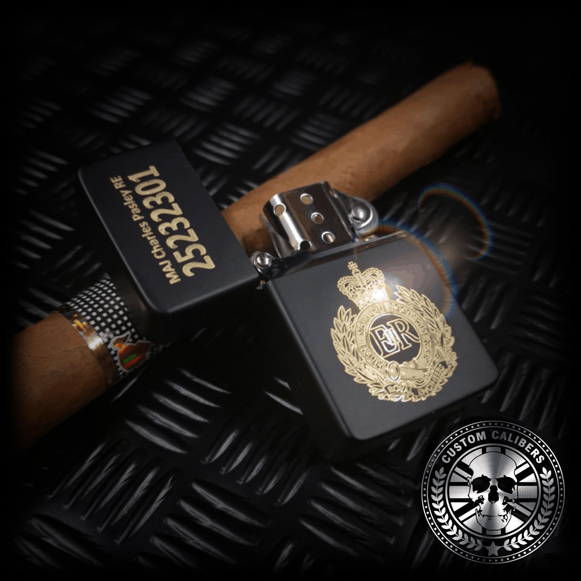 A matt black lighter with the lid open engraved with the royal engineers crest resting on a cuban cigar