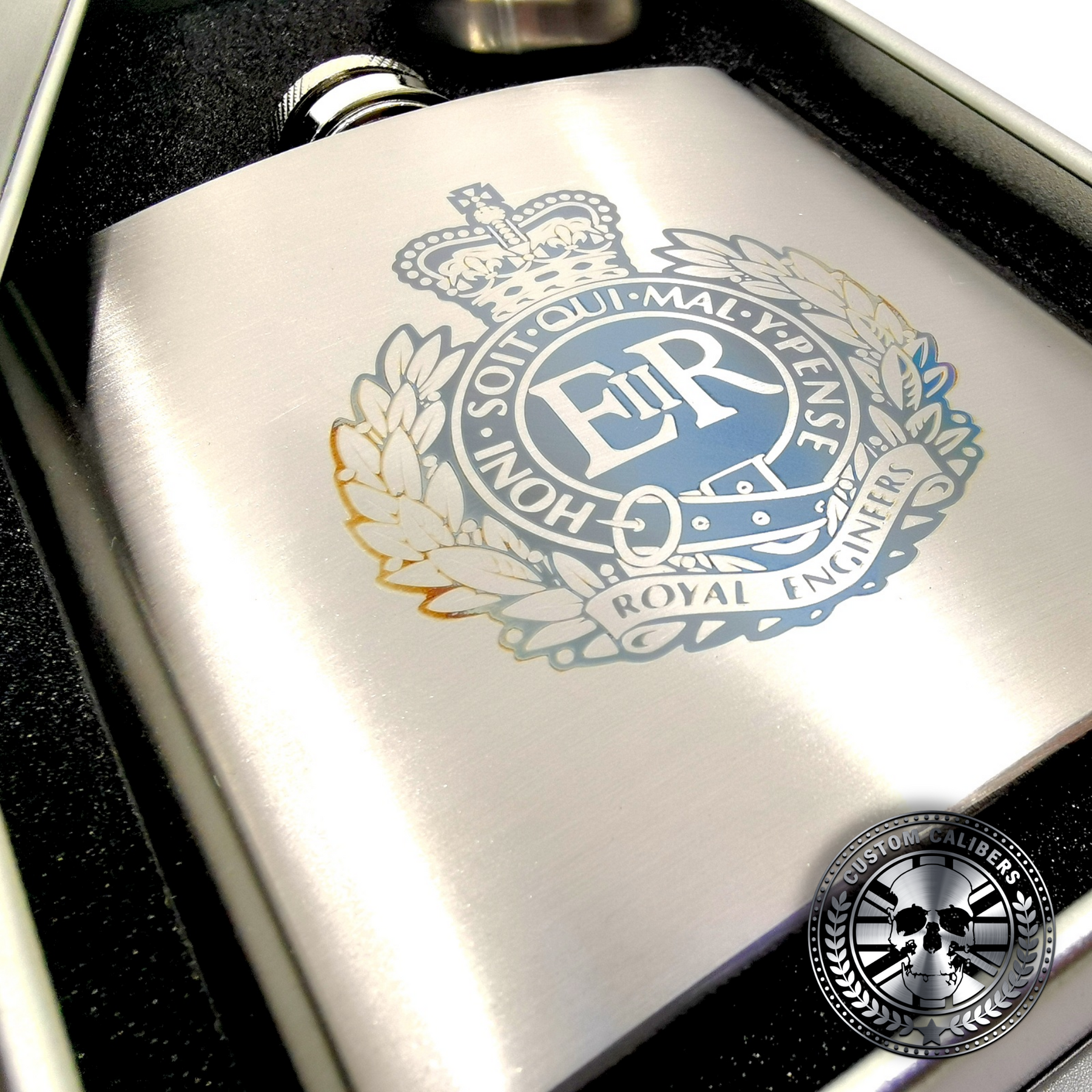 a brushed stainless steel hip flask engraved with a military crest